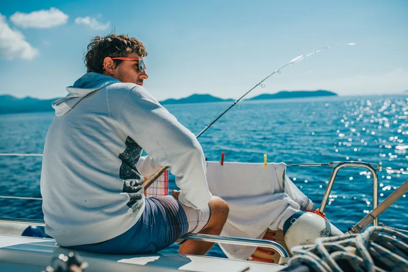 Un homme assis sur un bateau regarde une canne à pêche