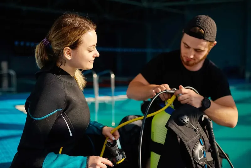 Deux personnes en combinaison de plongée vérifient l'équipement près d'une piscine