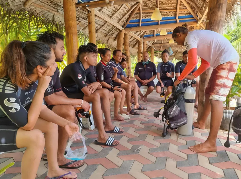 Groupe de plongeurs en formation, assis et écoutant un instructeur