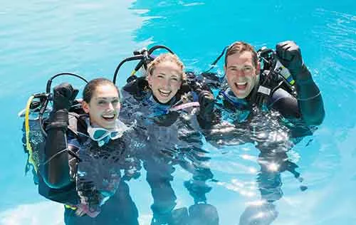 Trois plongeurs souriants, équipés, dans une eau claire et ensoleillée