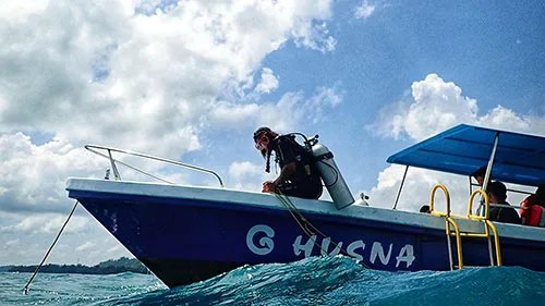 Plongeur s'équipant sur un bateau bleu sous un ciel nuageux