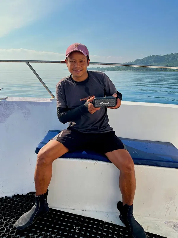 Un homme souriant sur un bateau, tenant un haut-parleur Marshall