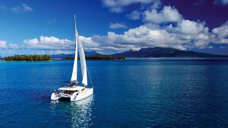Catamaran à voile naviguant sur une mer bleue sous un ciel nuageux