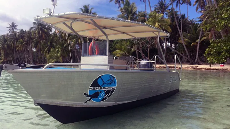 Bateau de plongée gris avec auvent sur une eau turquoise claire