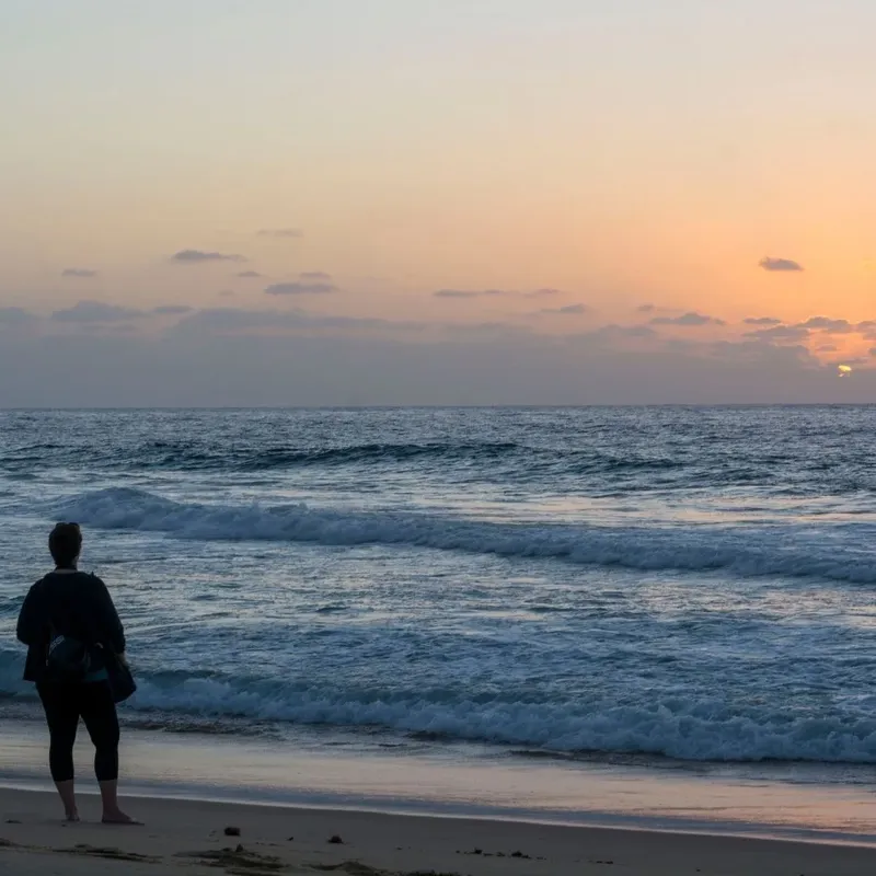 Personne debout sur une plage regardant l'océan au coucher du soleil