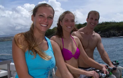 Trois personnes souriantes sur un bateau de plongée en mer