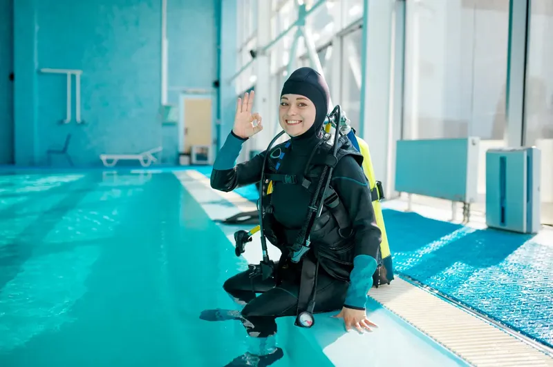 Plongeuse en combinaison, souriante, faisant un signe OK au bord d'une piscine