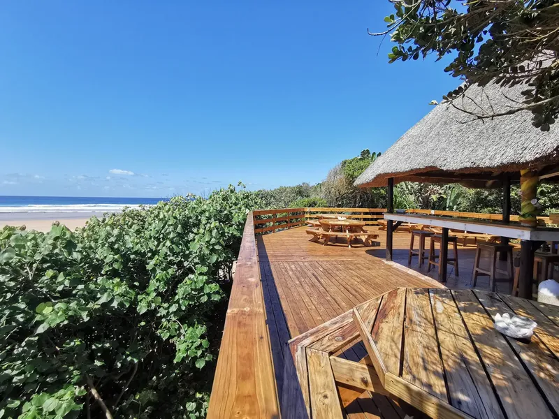 Terrasse en bois avec tables, chaises et vue sur la mer et végétation