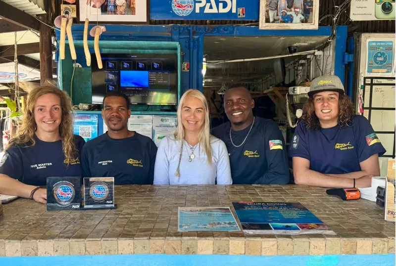 Cinq membres du personnel souriants posent devant le comptoir d'accueil