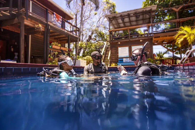 Trois plongeurs en formation dans une piscine, équipement complet visible