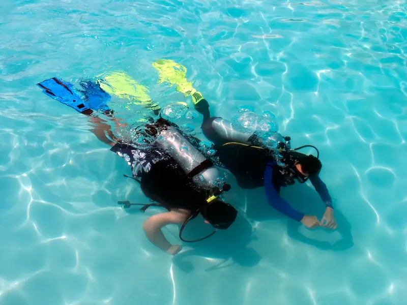 Deux plongeurs s'entraînent en piscine, équipement complet, eau turquoise claire