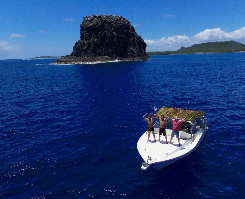 Trois personnes sur un bateau en mer devant un rocher volcanique