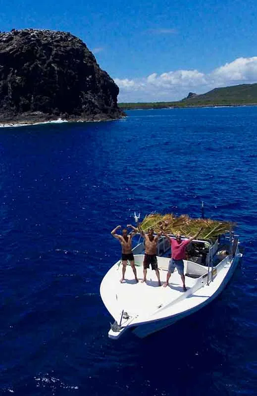 Trois personnes sur un bateau en mer, côte rocheuse en arrière-plan
