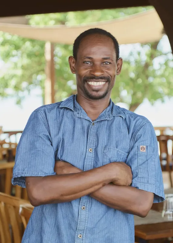 Homme souriant, bras croisés, chemise bleue, portrait en extérieur