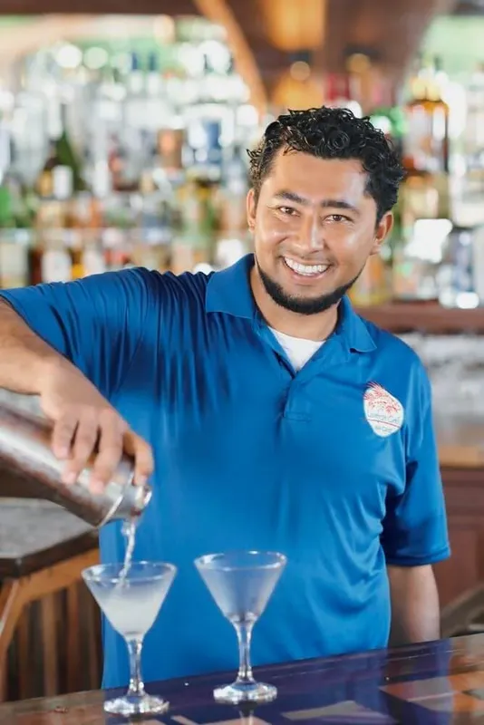 Un homme souriant prépare des cocktails derrière un comptoir de bar
