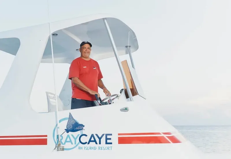 Homme souriant au volant d'un bateau blanc avec logo Ray Caye