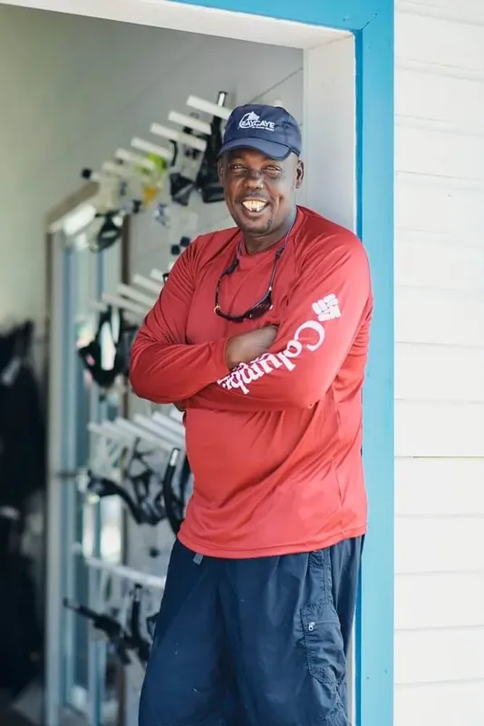 Homme souriant bras croisés devant équipement de plongée et gilets