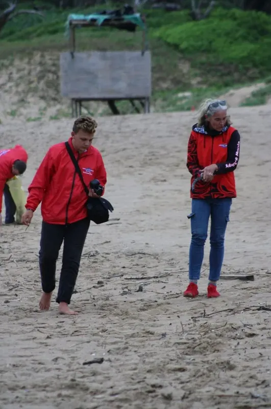 Deux personnes marchent sur une plage de sable, vêtues de manière décontractée