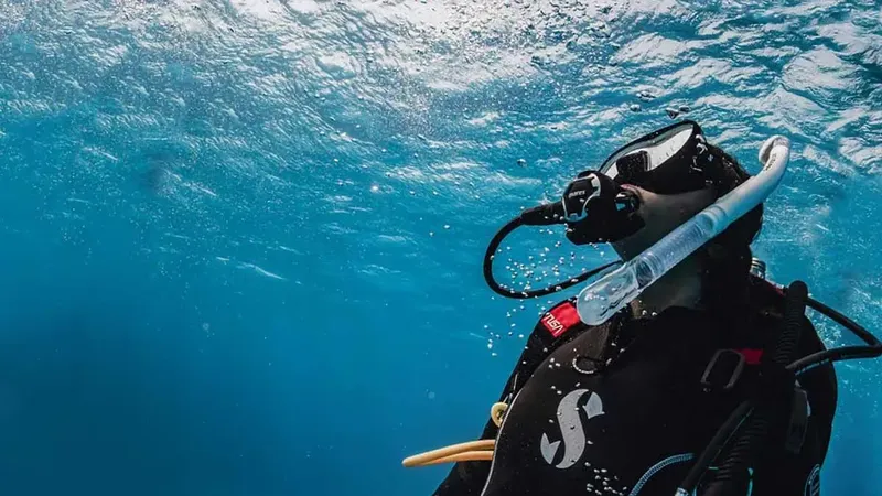 Plongeur en scaphandre noir nageant dans une eau bleue claire