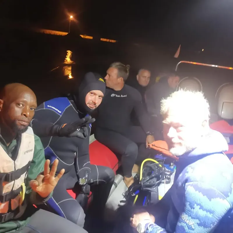 Trois plongeurs équipés discutent sur un bateau, sourires et gestes