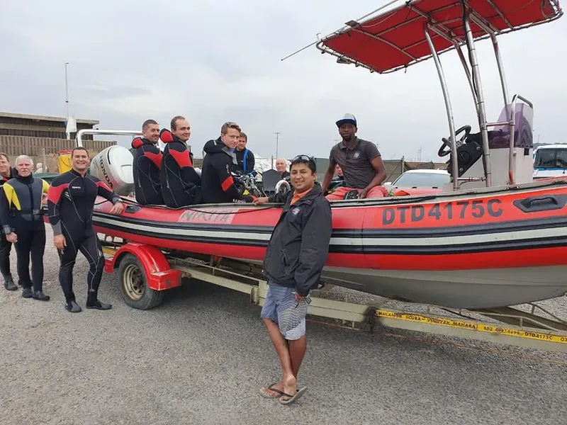 Groupe de plongeurs et un instructeur posent devant un semi-rigide rouge
