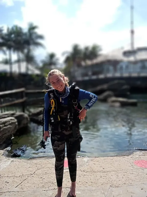 Plongeuse souriante en combinaison, gilet et bouteille sur un quai