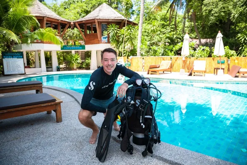 Un plongeur souriant pose avec son équipement près d'une piscine