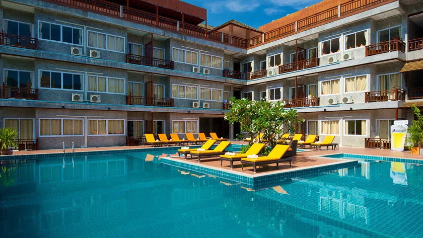 Bâtiment avec balcons, piscine turquoise et chaises longues jaunes