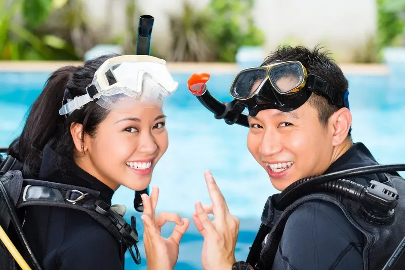 Deux plongeurs souriants avec leur équipement près d'une piscine