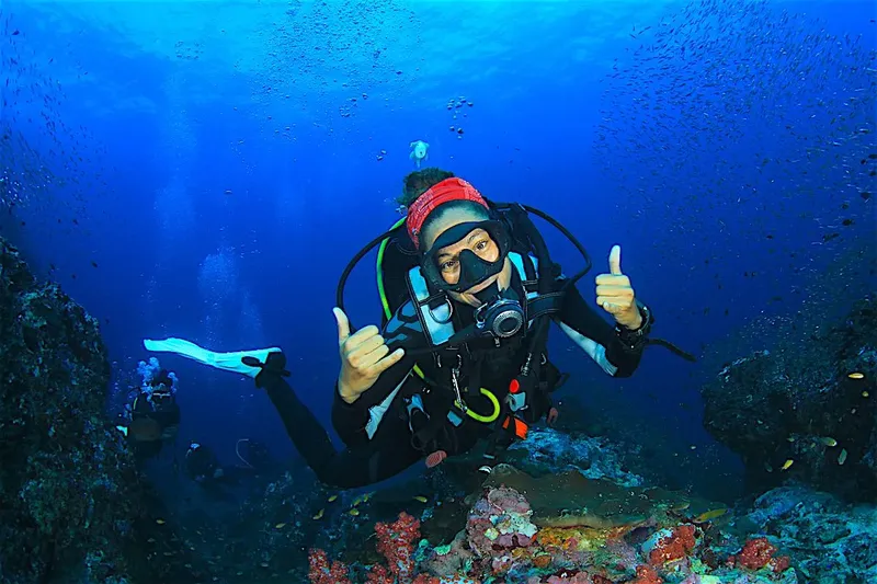 Plongeuse souriante avec signe OK entourée de petits poissons bleus