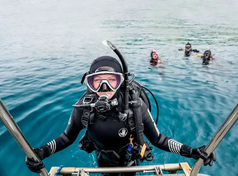 Plongeuse souriante au bord d'un bateau avec d'autres plongeurs