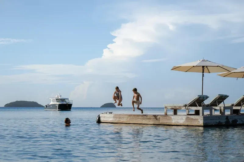 Des personnes sautent d'un ponton dans une eau calme et bleue