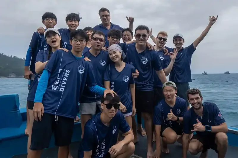 Groupe de personnes souriantes sur un bateau en mer, portant des t-shirts