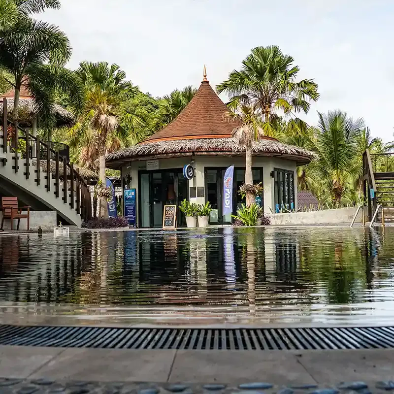 Petit bâtiment avec toit conique et enseignes devant une piscine