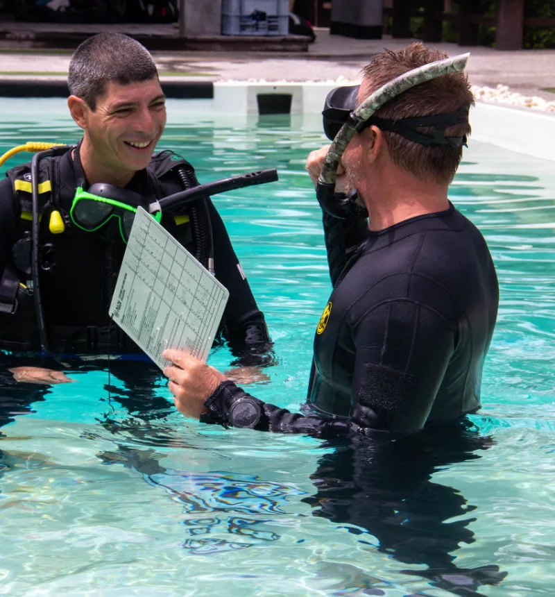 Deux plongeurs en combinaison discutent d'une tablette dans une piscine