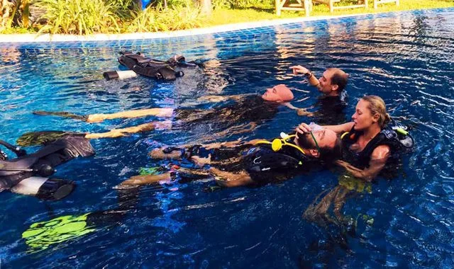 Trois personnes en combinaison de plongée s'entrainent dans une piscine