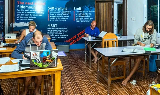 Trois personnes travaillent sur des ordinateurs dans une salle de cours
