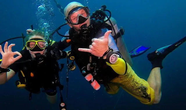 Deux plongeurs souriants font des signes de la main sous l'eau