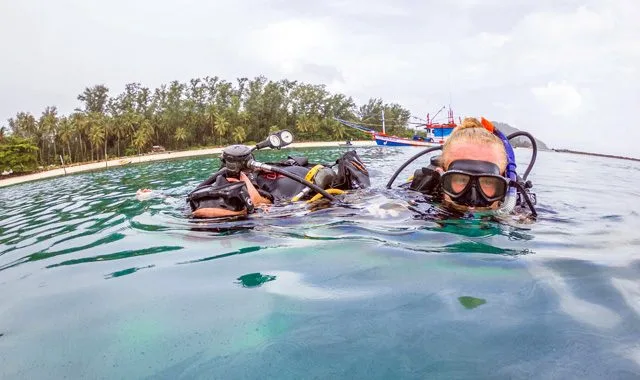 Deux plongeurs en surface, équipés, regardent vers l'objectif dans l'eau turquoise