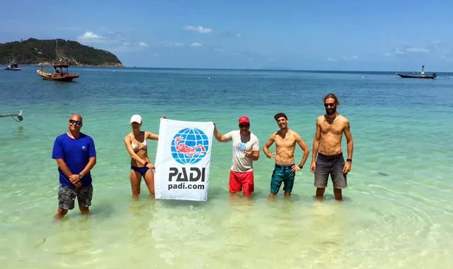 Groupe de personnes souriantes tenant un drapeau PADI dans l'eau