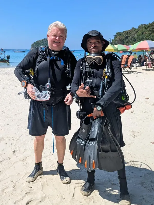 Deux plongeurs souriants sur une plage, équipés et prêts à plonger