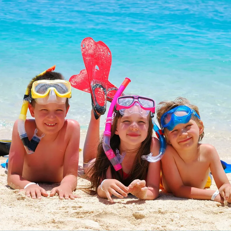 Trois enfants souriants sur une plage avec masque et tuba