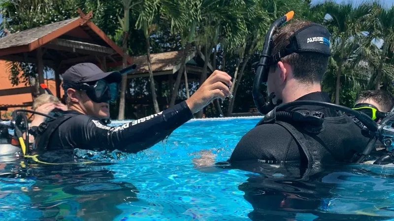 Deux plongeurs en formation dans une piscine, un instructeur aide l'autre