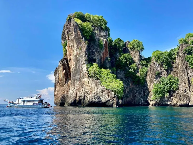 Bateau de plongee devant une falaise rocheuse couverte de végétation tropicale