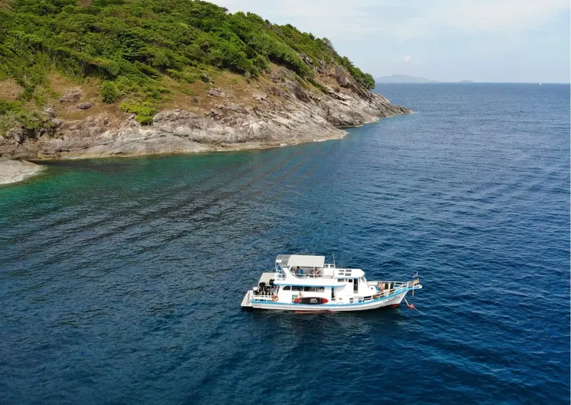 Bateau de plongée blanc et bleu navigue au large d'une côte rocheuse
