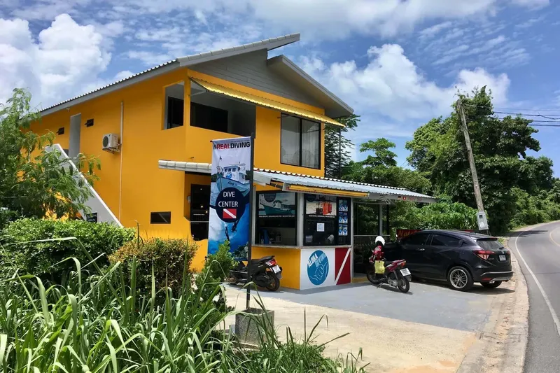 Façade jaune d'un centre de plongée avec enseigne et parking devant