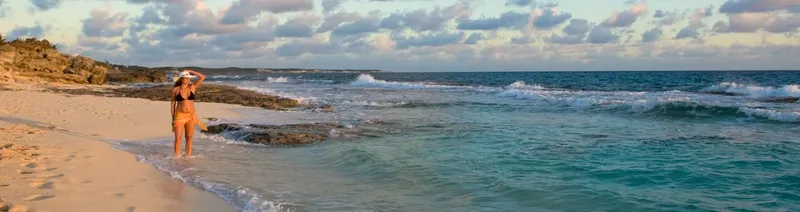 Femme sur une plage de sable fin, regardant l'océan turquoise
