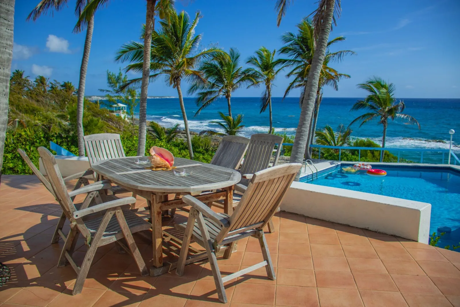 Terrasse avec mobilier en bois, piscine et vue sur mer tropicale