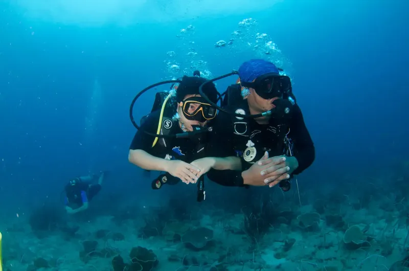 Deux plongeurs communiquent sous l'eau, avec des bulles et du sable