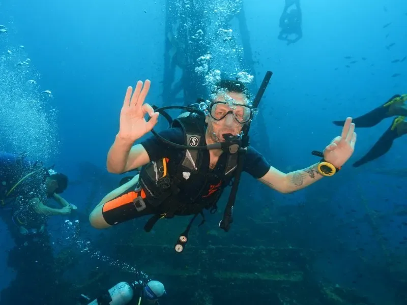 Plongeur souriant avec signe OK, entouré d'autres plongeurs en mer